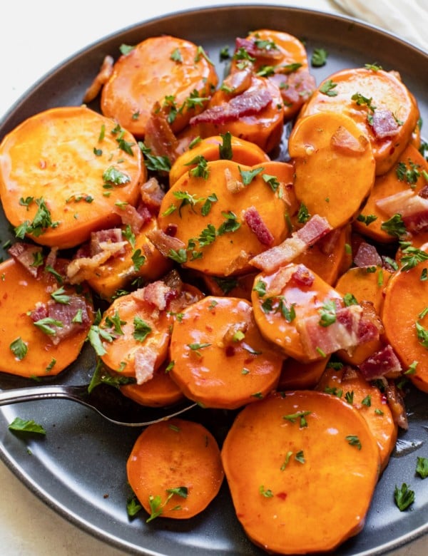 sweet potatoes on a blue plate topped with honey, bacon and parsley