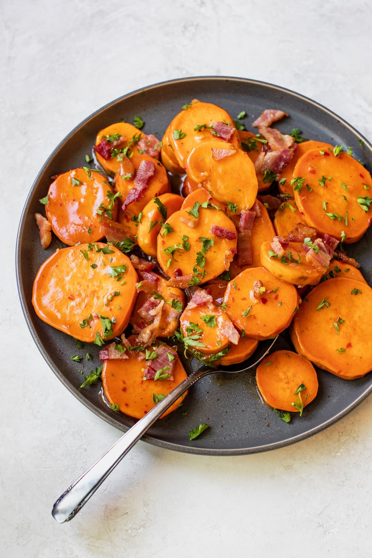 sweet potatoes on a blue plate topped with honey, bacon and parsley