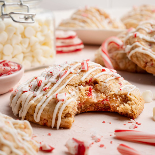 Close-up of a white chocolate peppermint cookie with a large bite taken out, showing the soft, chewy interior studded with white chocolate chips and peppermint pieces.