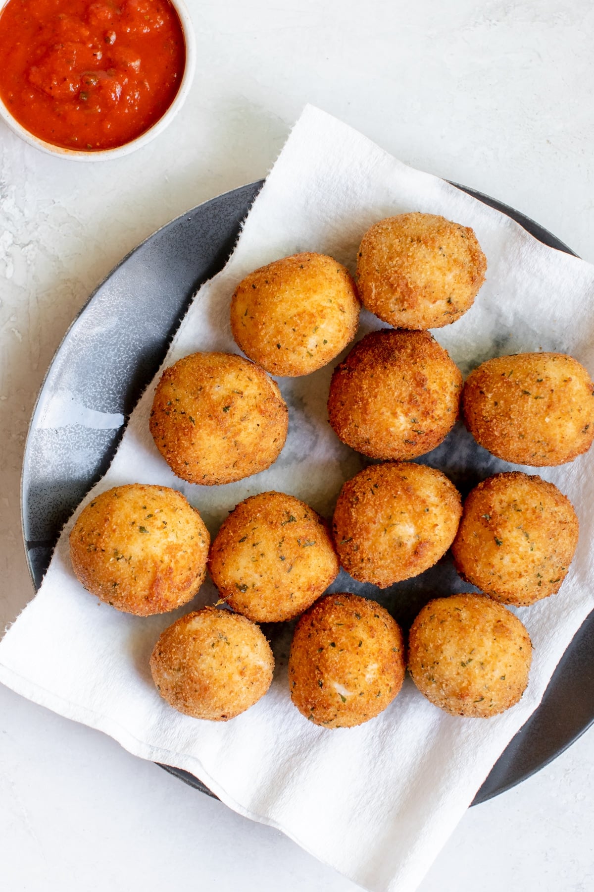 fried rice formed into balls on a blue plate on a paper towel with marinara on the side
