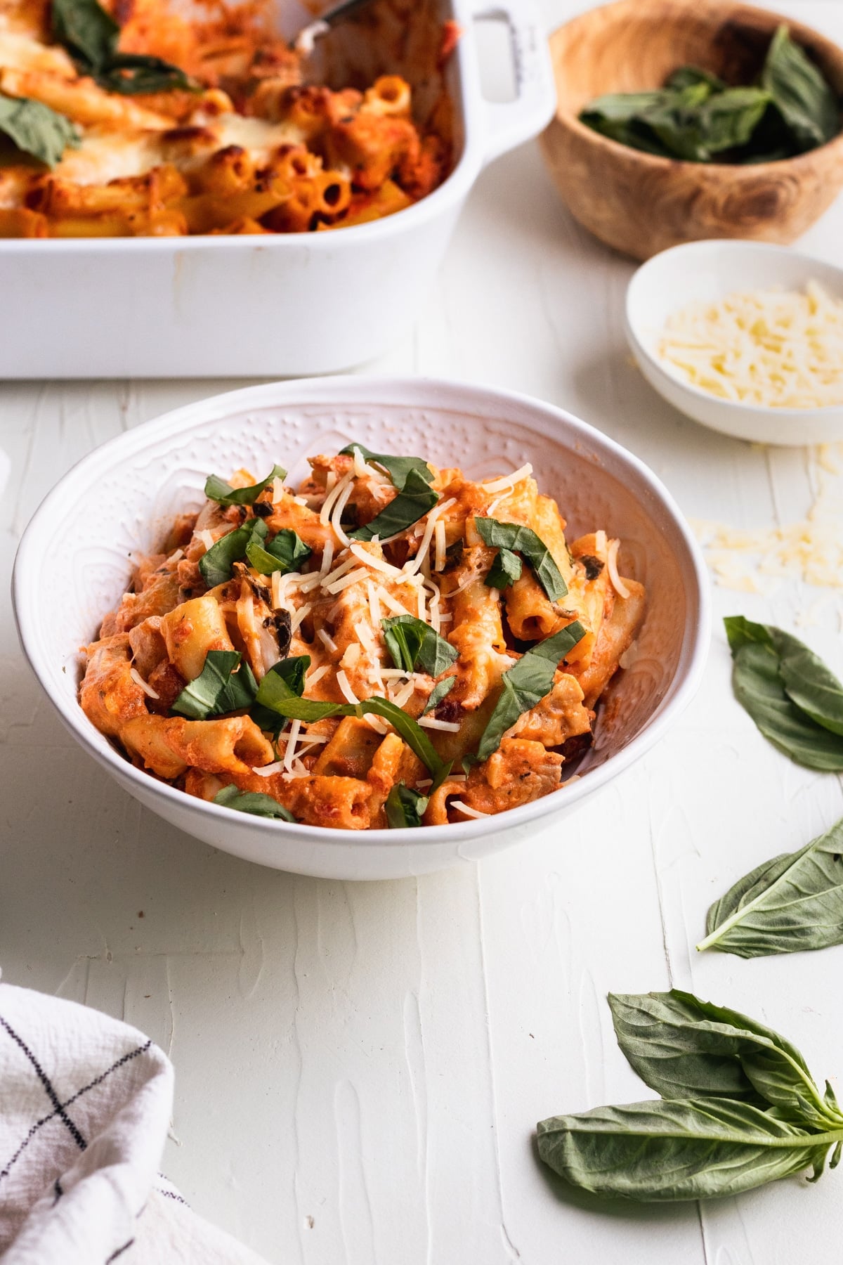 ziti casserole in a white bowl topped with basil and parmesan cheese