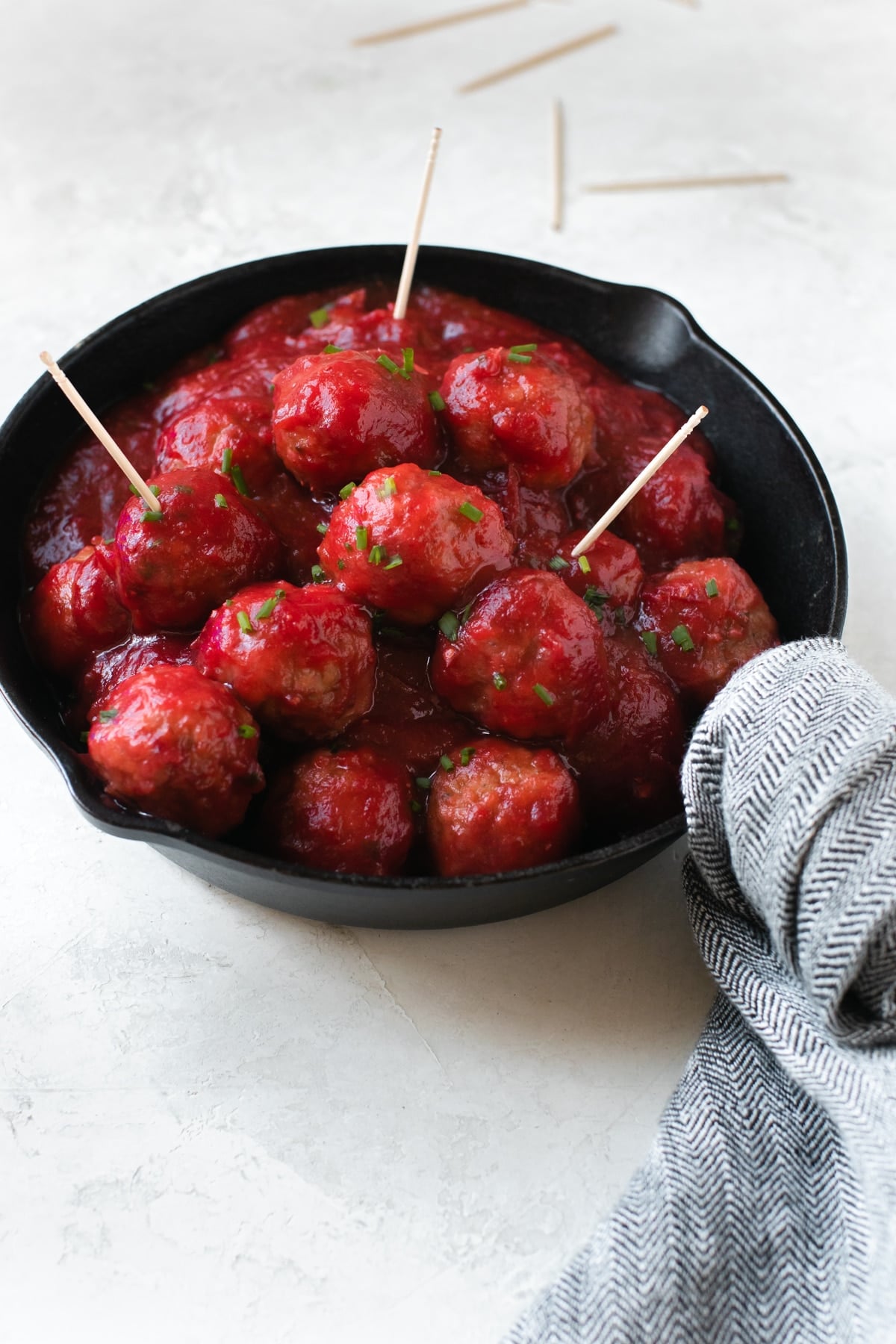 meatballs covered in cranberry sauce and garnished with chives in a cast iron skillet