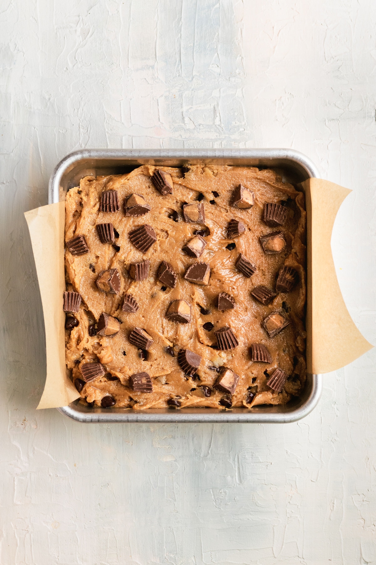 blondie batter in a square baking pan topped with Reese's peanut butter cups chopped into small pieces