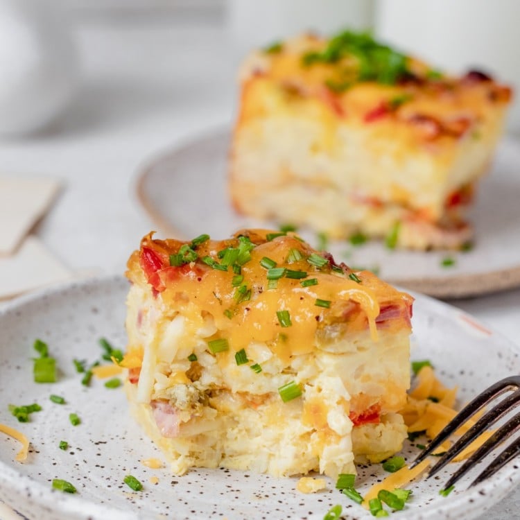 a slice of an egg casserole on a speckled plate with milk in the background