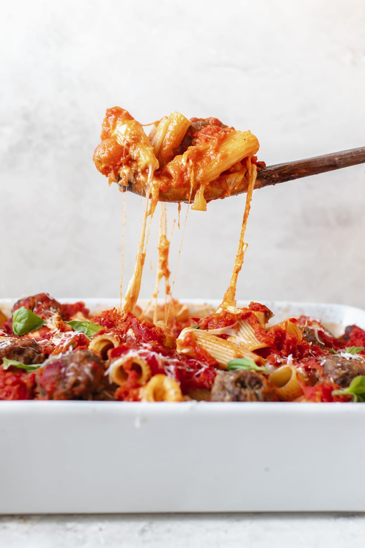 a wooden spoon scooping out pasta from a white casserole dish