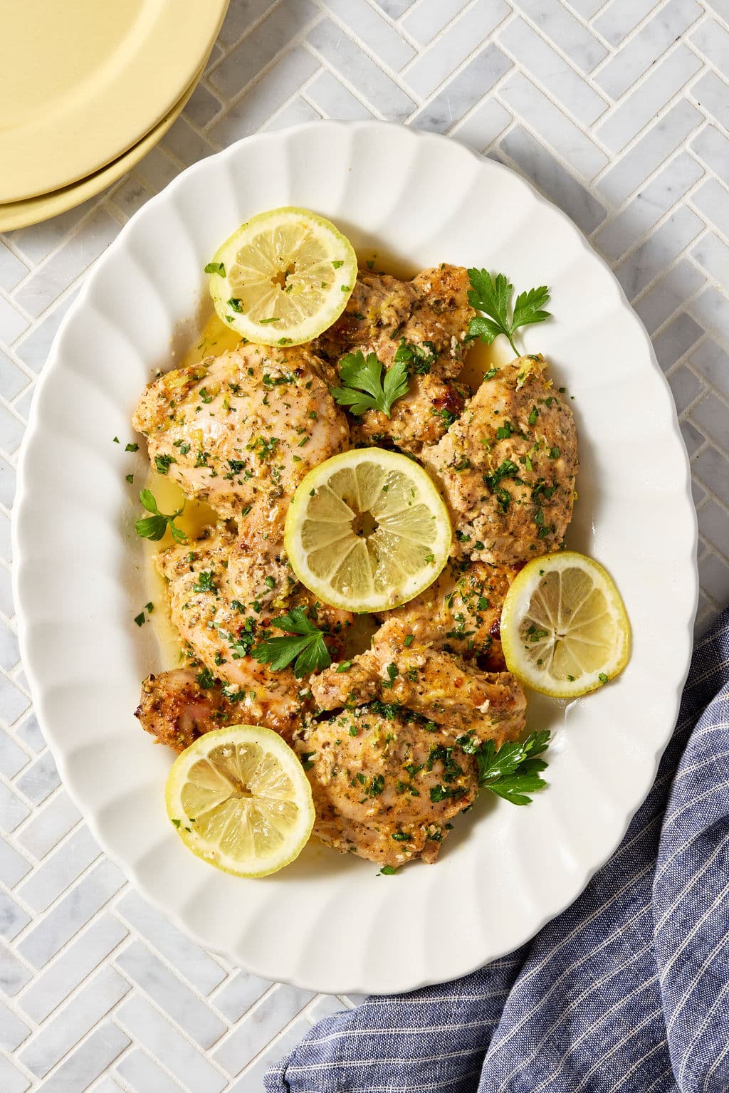 Platter of baked Greek yogurt lemon chicken topped with fresh parsley, lemon zest, and lemon slices, served with flavorful pan juices spooned over the chicken.