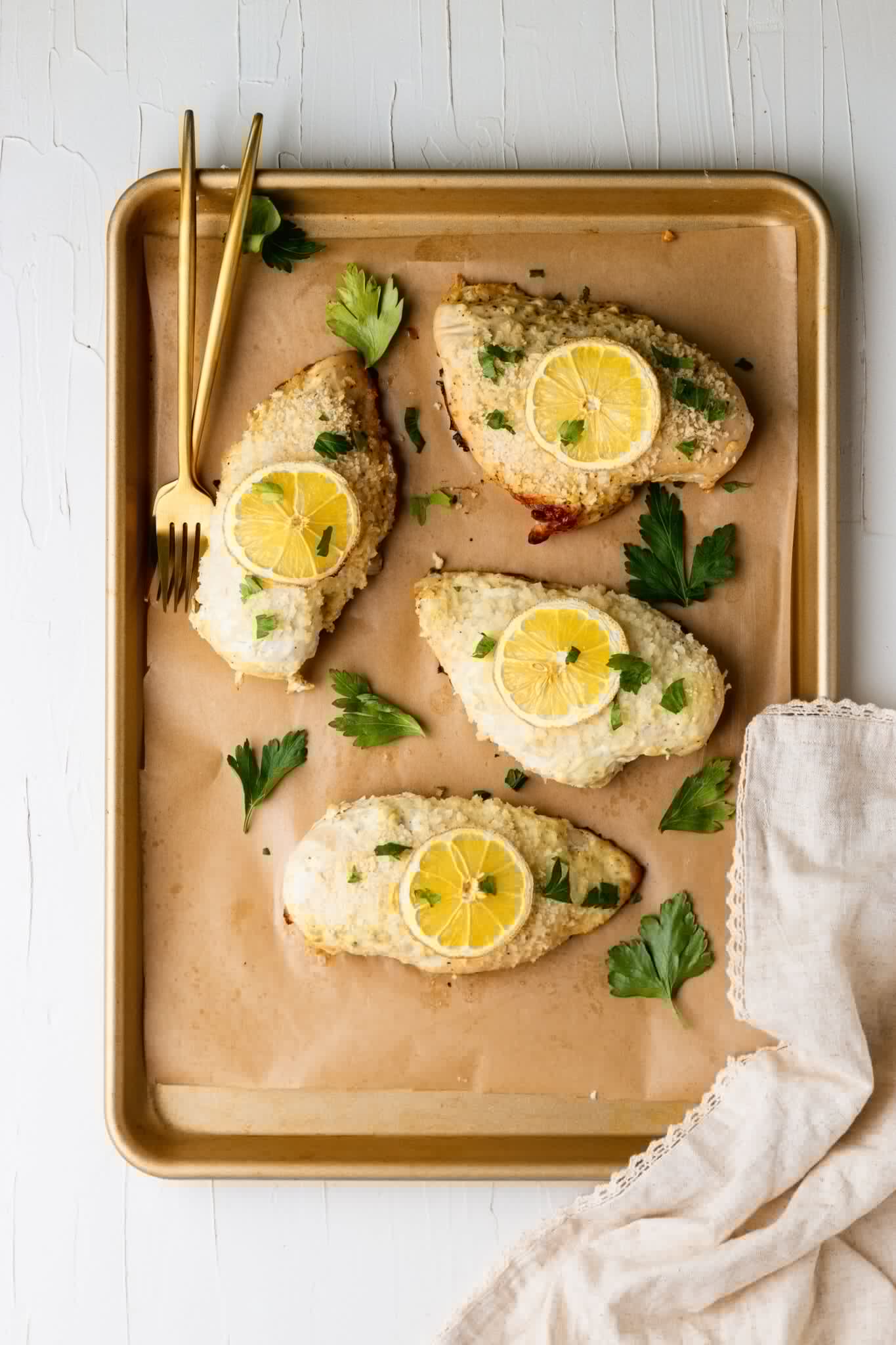 baked chicken on a sheet pan lined with parchment paper and a lemon slice