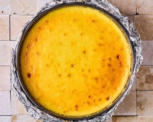 Round cheesecake in a pie pan lined with foil, after coming out of hte oven.