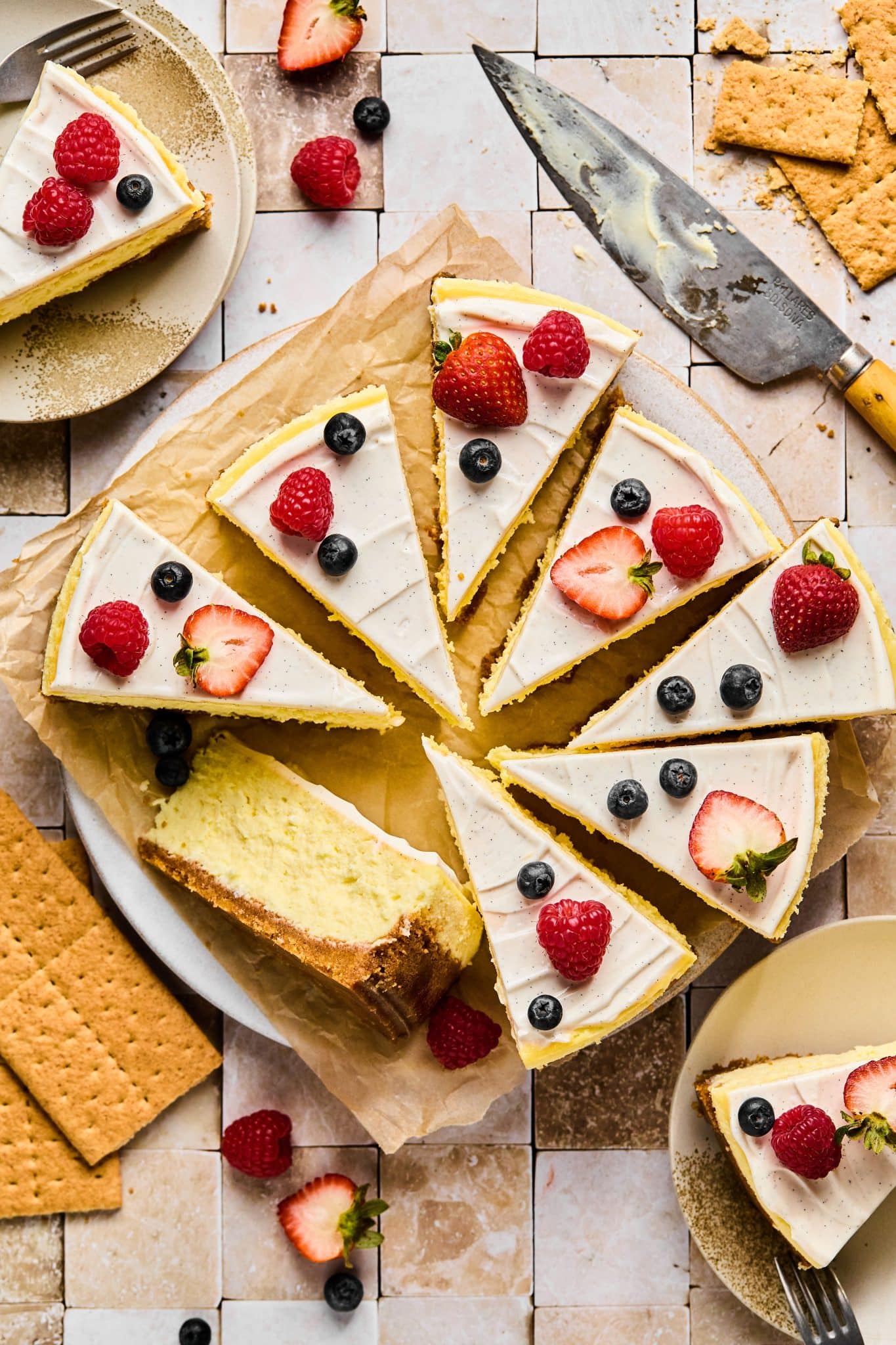 Full cheesecake topped with vanilla frosting cut into pieces, topped with berries.