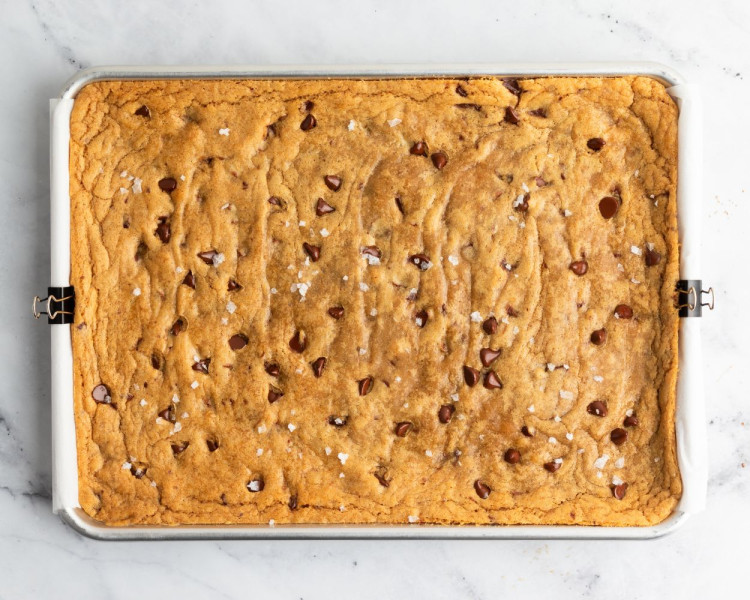 Freshly baked tray of golden brown blondies in a rectangular pan, studded with chocolate chips and sprinkled with flaky sea salt.