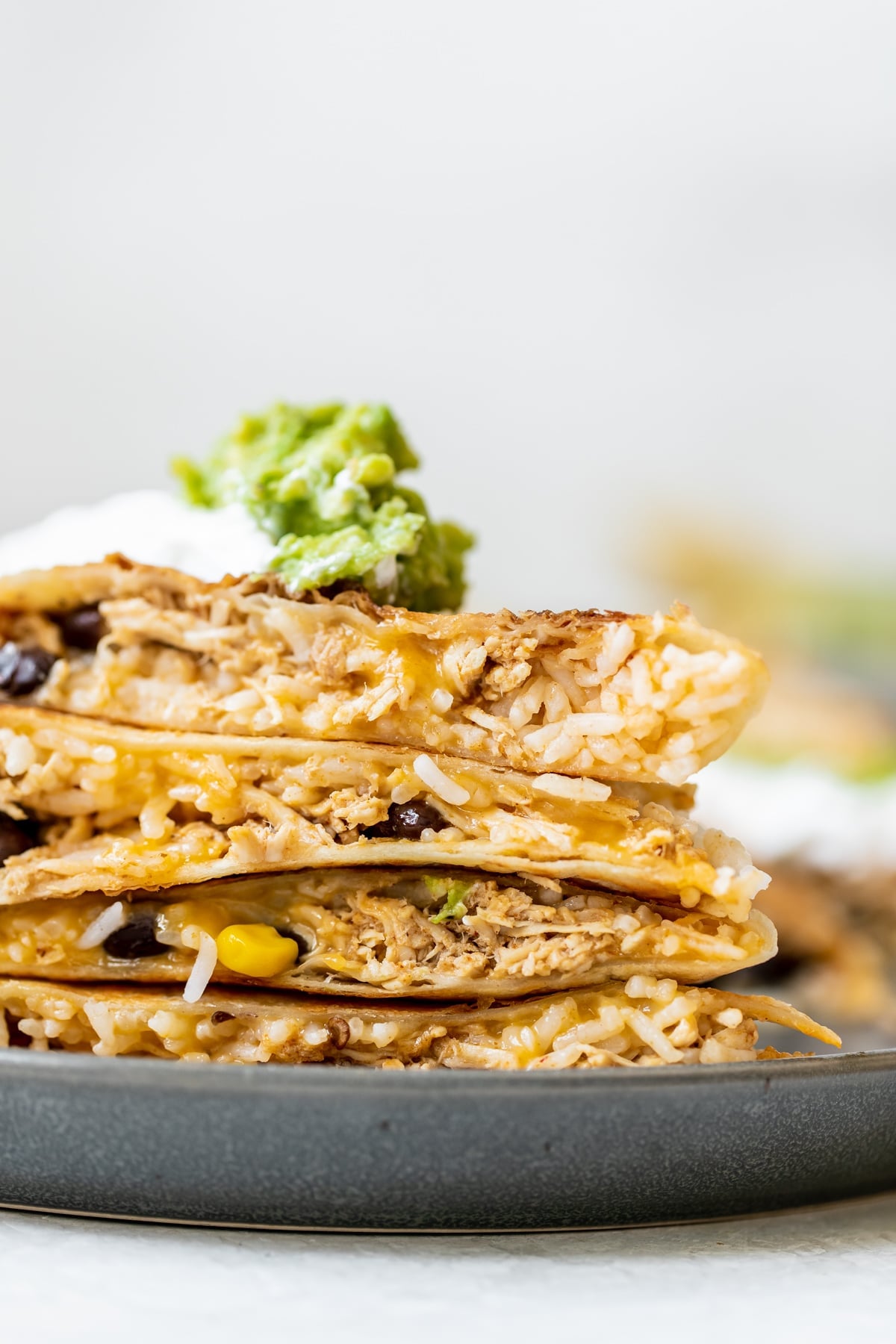 chipotle chicken quesadilla cut in half and stacked on top of each other topped with sour cream and guacamole 