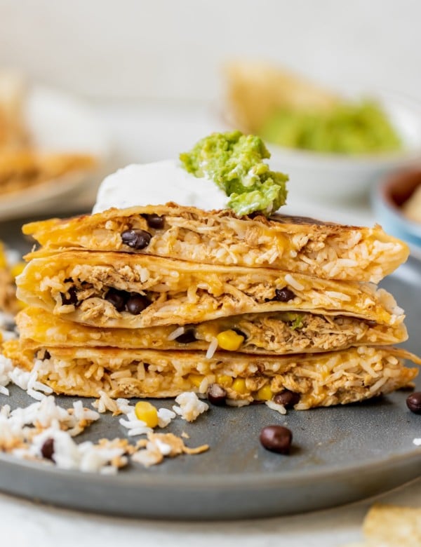 chipotle chicken quesadilla cut in half and stacked on top of each other topped with sour cream and guacamole