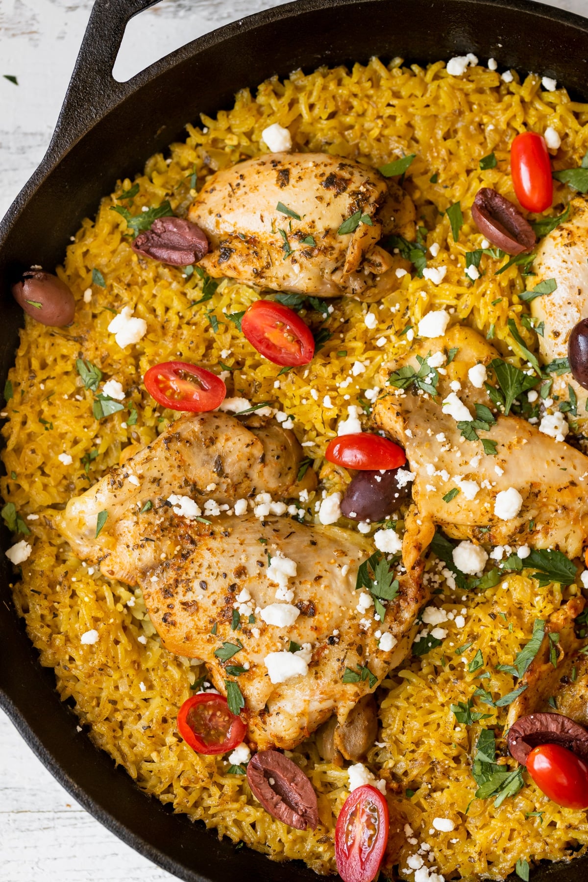 mediterranean chicken and rice in a cast iron skillet garnished with kalamata olives and feta cheese