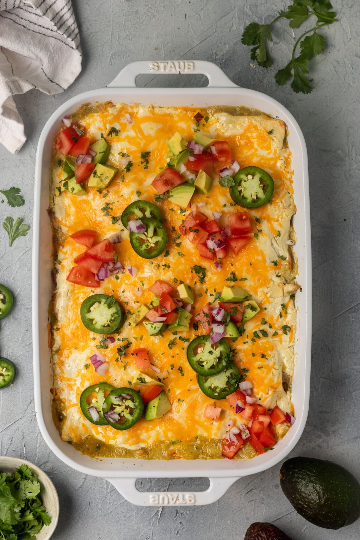 a casserole in a white casserole dish garnished with jalapenos, tomatoes and cilantro.