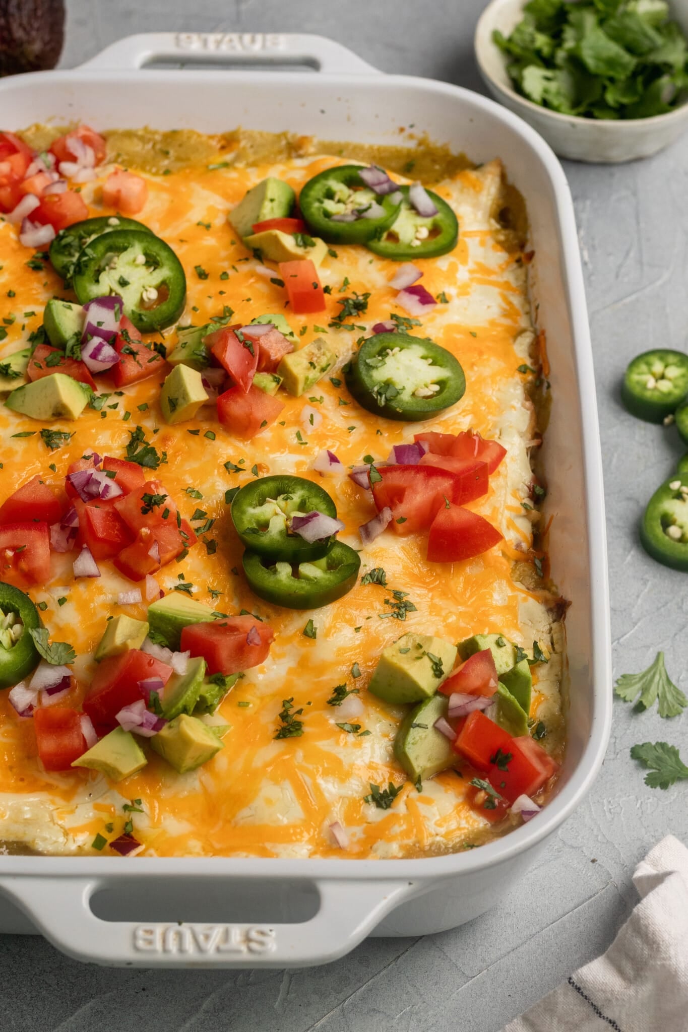 a casserole in a white casserole dish garnished with jalapenos, tomatoes and cilantro.