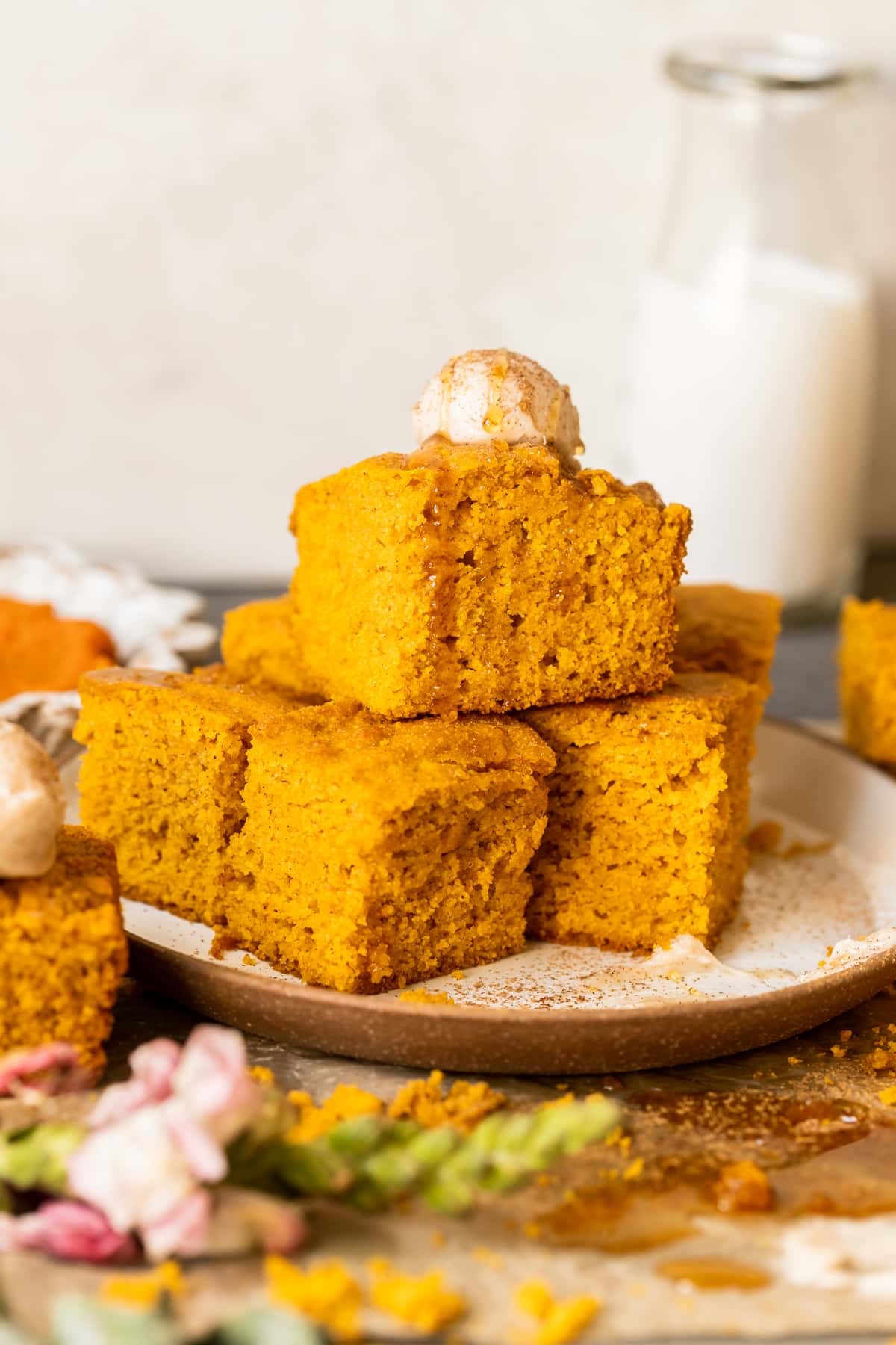 squares of pumpkin cornbread stacked on a tan plate and topped with a scoop of butter and a drizzle of honey