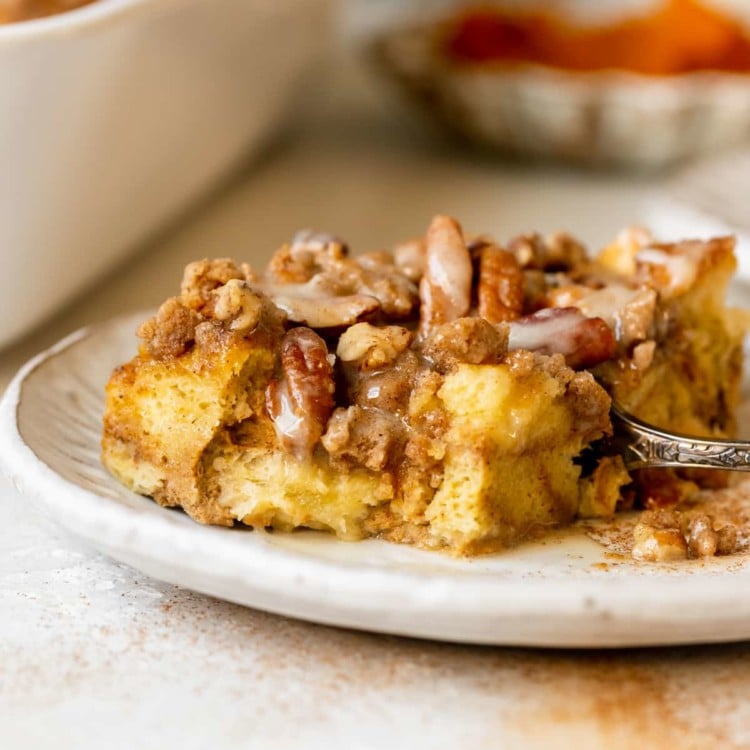 french toast made with pumpkin on a white plate topped with a brown sugar pecan streusel and maple glaze.