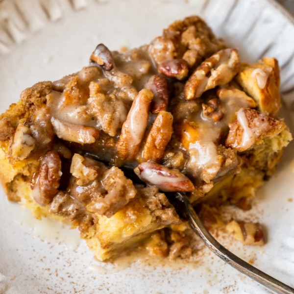 french toast made with pumpkin on a white plate topped with a brown sugar pecan streusel and maple glaze.