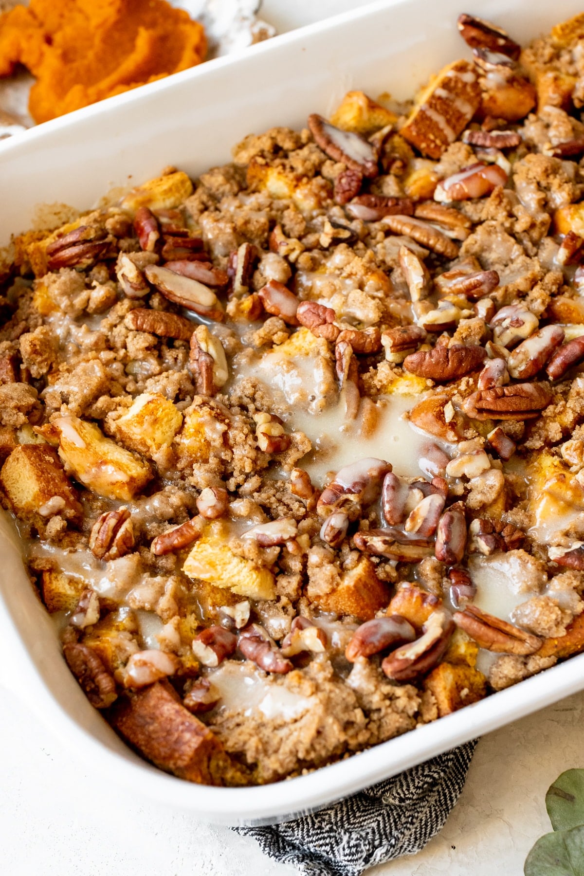 french toast in a white casserole dish topped with a brown sugar streusel and pecans and a maple syrup glaze. 