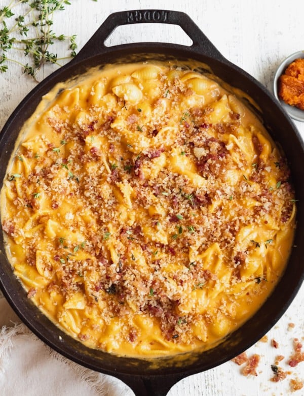 macaroni pasta on in a black cast iron skillet in a pumpkin cheddar cheese sauce garnished with bacon and fresh thyme.