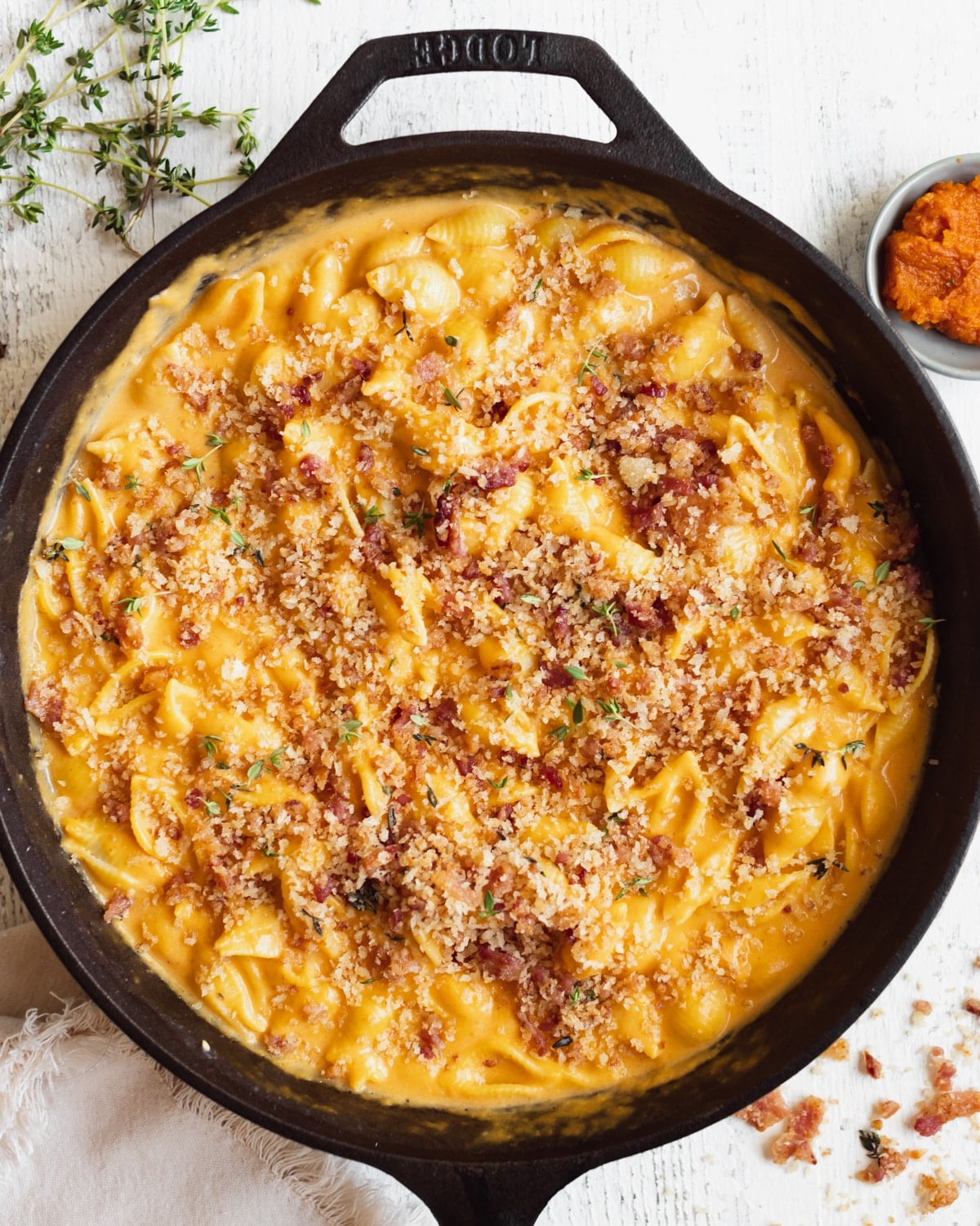 macaroni pasta on in a black cast iron skillet in a pumpkin cheddar cheese sauce garnished with bacon and fresh thyme.