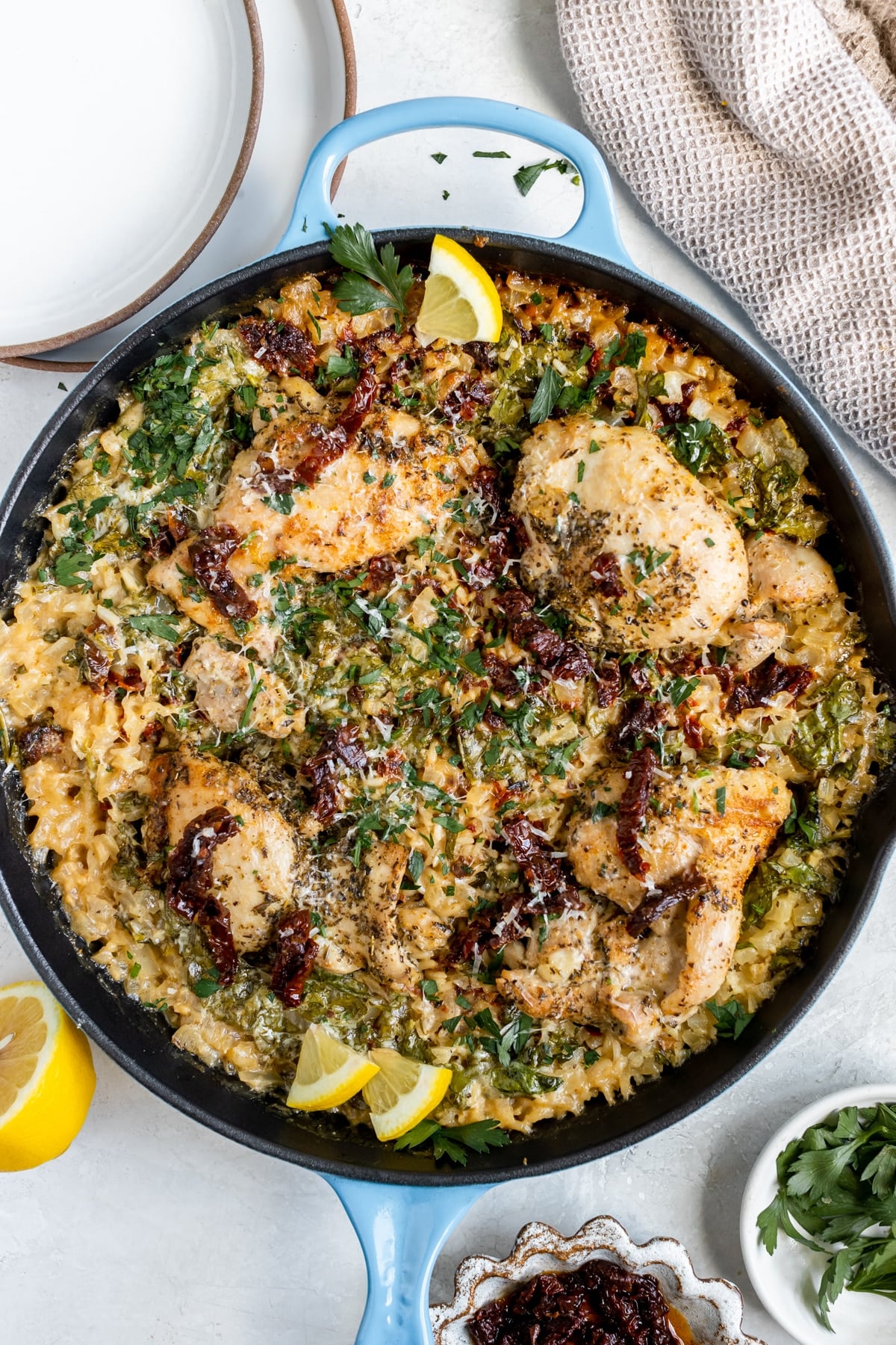 chicken and rice in a large cast iron skillet garnished with parmesan cheese, sun dried tomatoes, parsley and lemon slices. 
