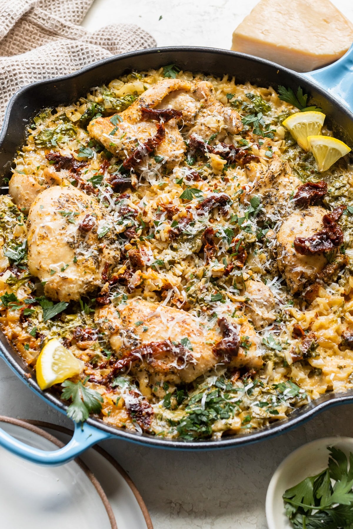 chicken and rice in a large cast iron skillet garnished with parmesan cheese, sun dried tomatoes, parsley and lemon slices. 