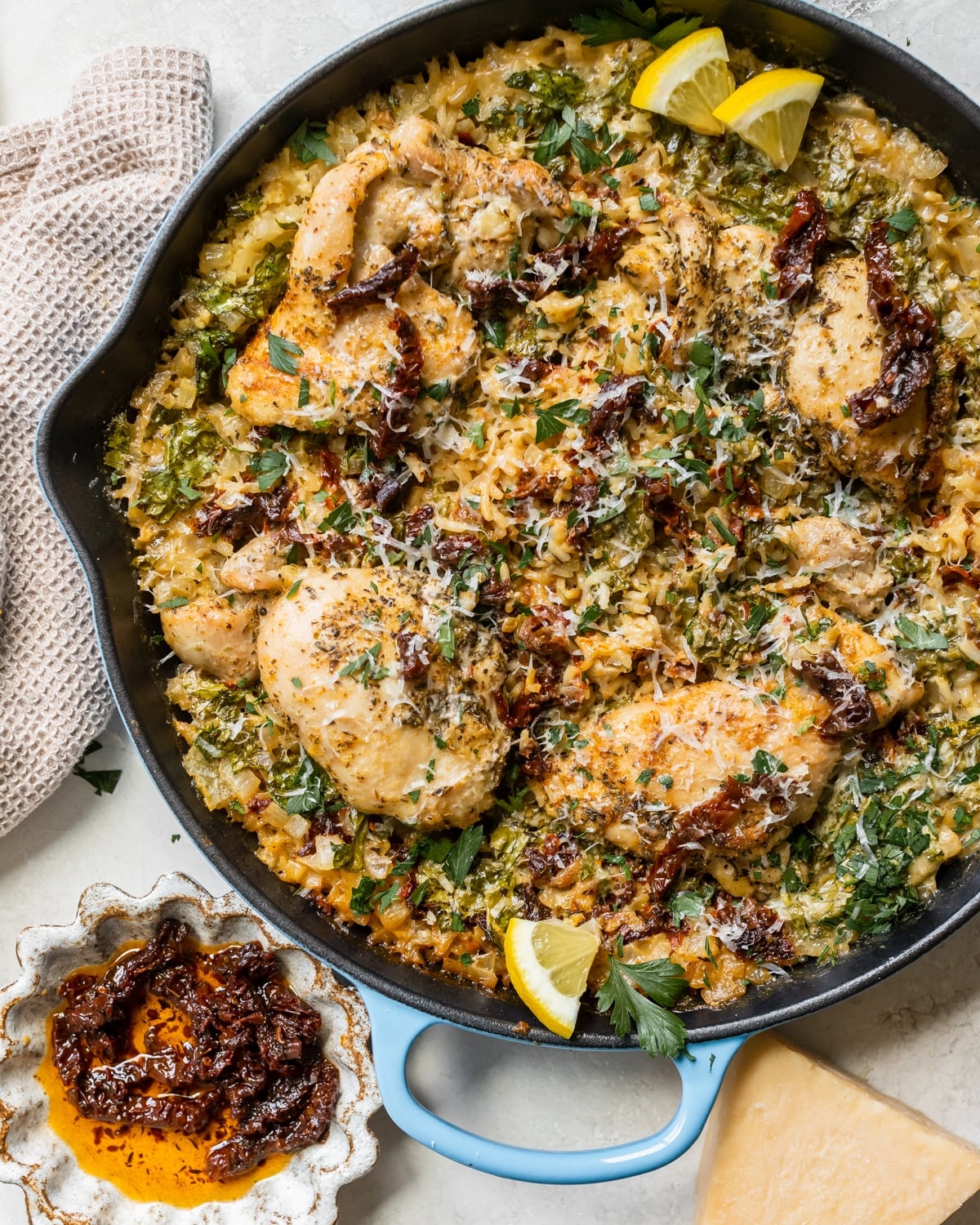 chicken and rice in a cast iron skillet garnished with parmesan cheese, sun dried tomatoes, parsley and lemon slices.