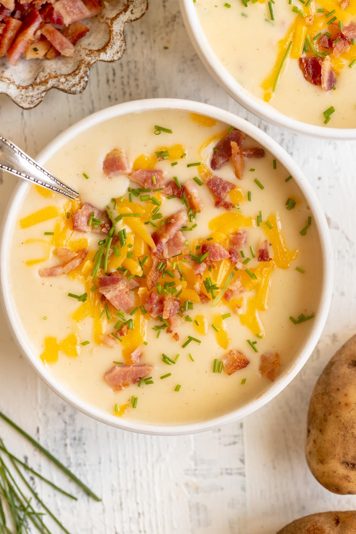 baked potato soup in a white bowl garnished with bacon, cheese and chives. 