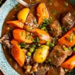 stew made with beef, potatoes and carrots in a blue bowl garnished with fresh chopped chives.