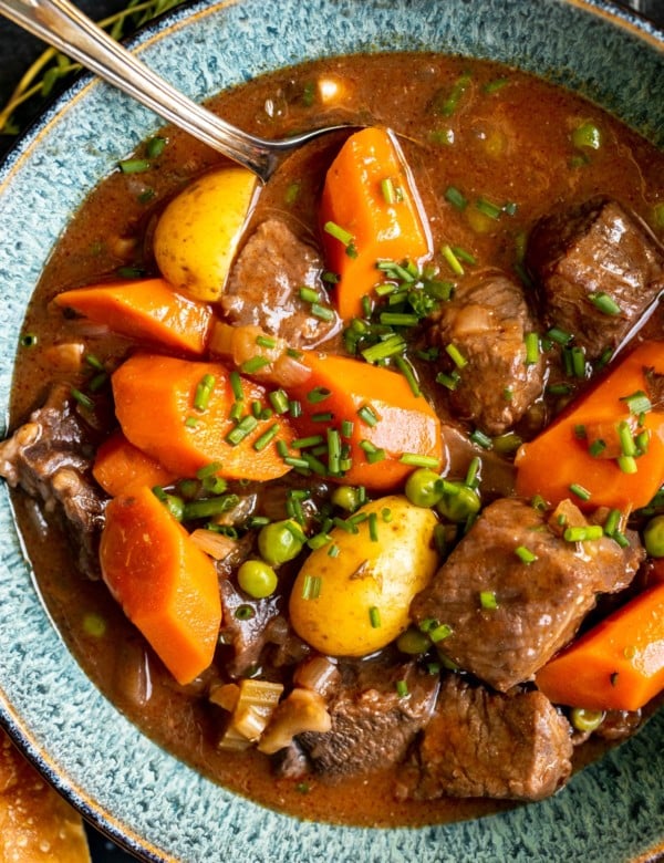 stew made with beef, potatoes and carrots in a blue bowl garnished with fresh chopped chives.