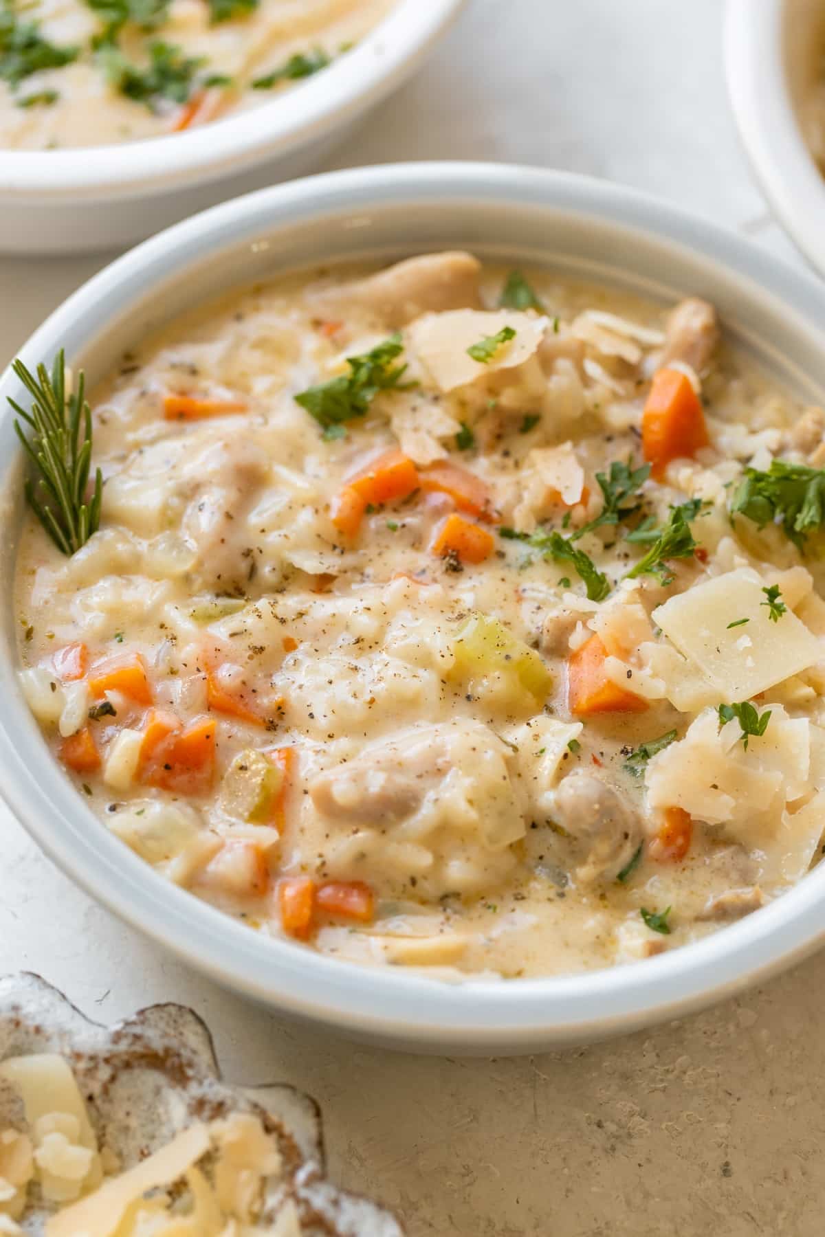chicken rice soup in a bowl garnished with parmesan cheese, black pepper and fresh parsley.