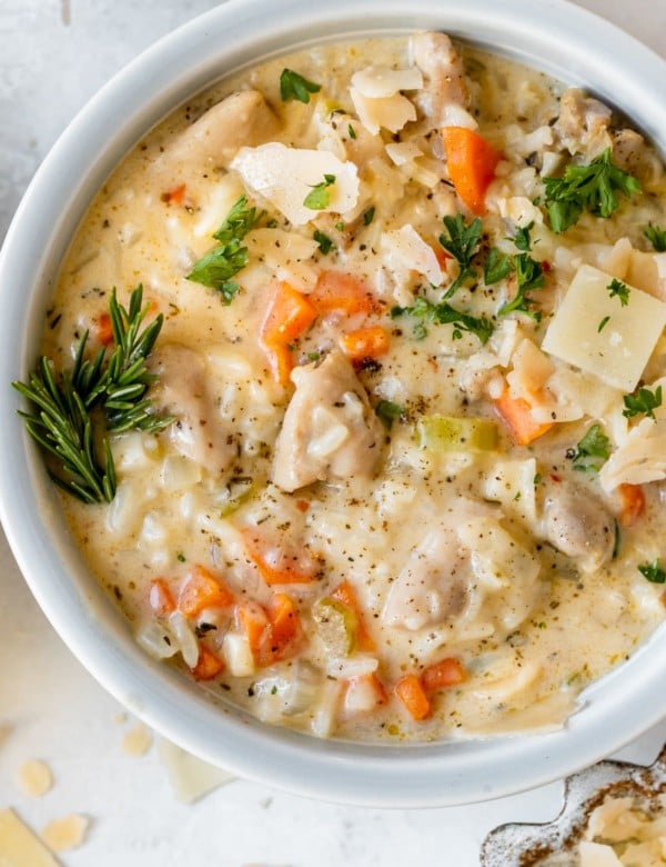 chicken rice soup in a bowl garnished with parmesan cheese, black pepper and fresh parsley.