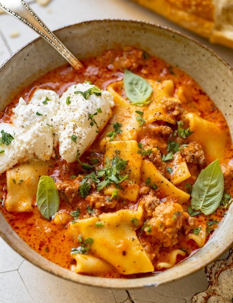 soup made with lasagna noodles in a bowl garnished with ricotta, parsley, basil and parmesan cheese.