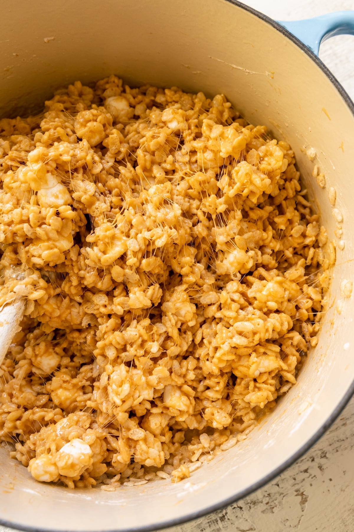 a wooden spoon stirring rice krispies in a dutch oven.