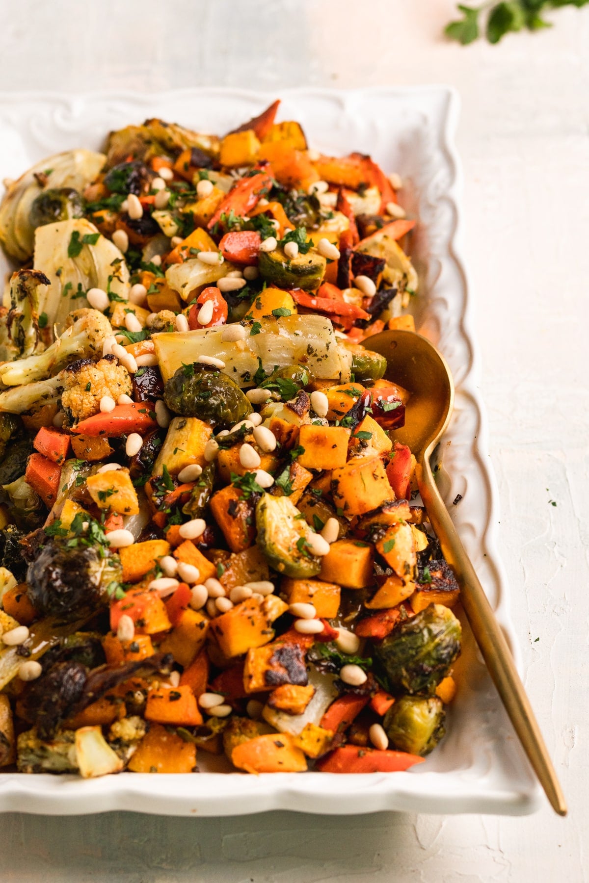 roasted veggies garnished with pine nuts on a white glass platter. 
