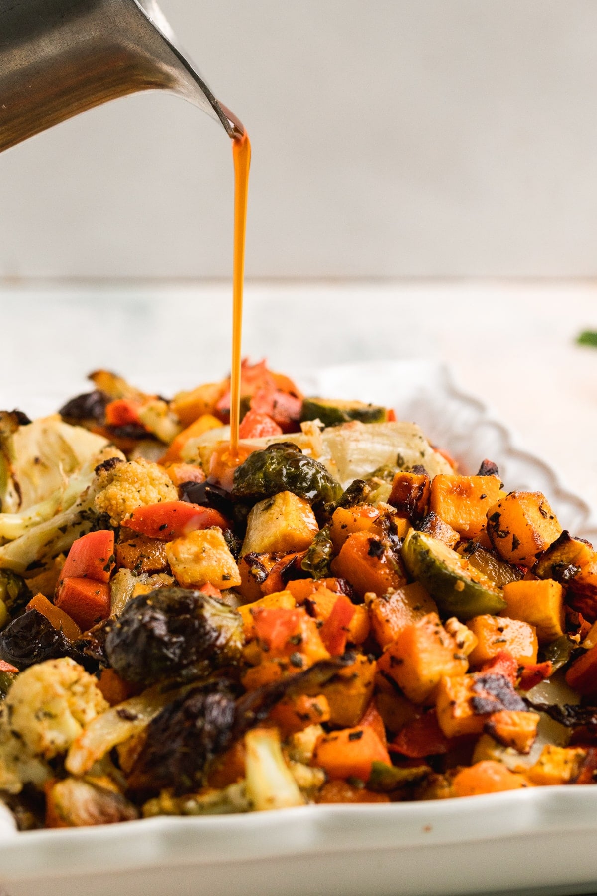 cider glaze being poured on a platter of roasted veggies. 