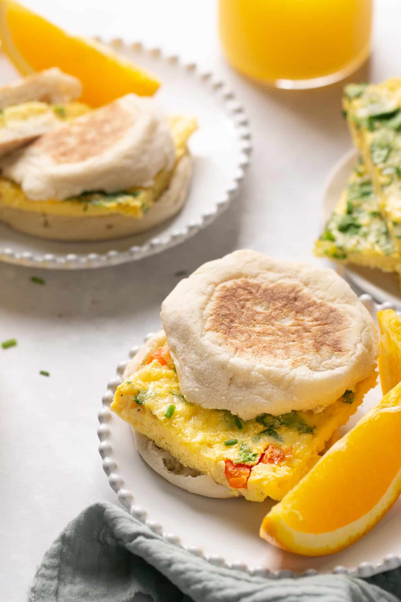 an english muffin with eggs on it on a white plate with an orange slice on the side. 