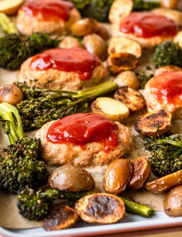 mini meatloaves topped with ketchen on a sheet pan surrounded by roasted broccoli and potatoes