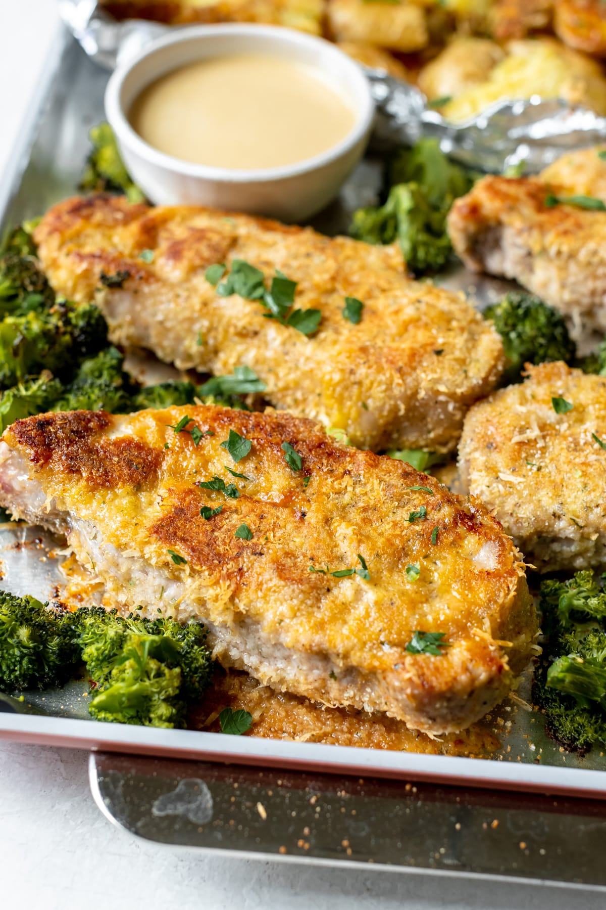 pork chop parmesan crusted on a sheet pan garnished with parsley. 