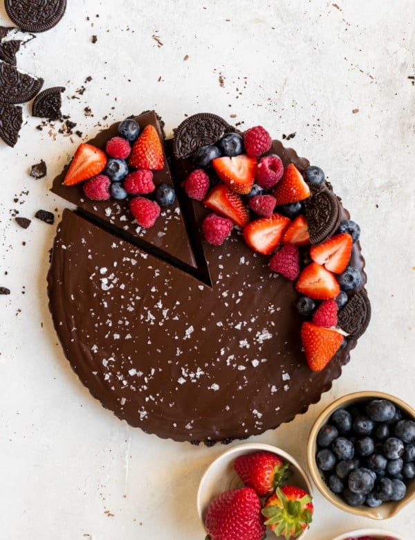 chocolate tart with one slice cut out, topped with berries and sea salt.