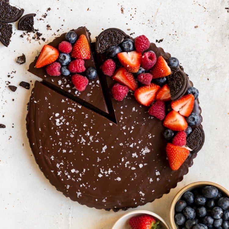 chocolate tart with one slice cut out, topped with berries and sea salt.