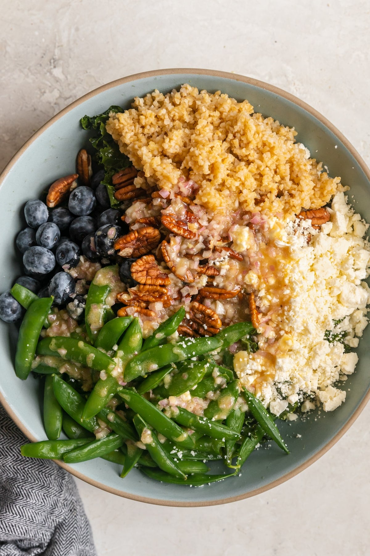 kale in a bowl with blueberries, pecans, bulgur wheat, feta cheese and dressing poured on top.