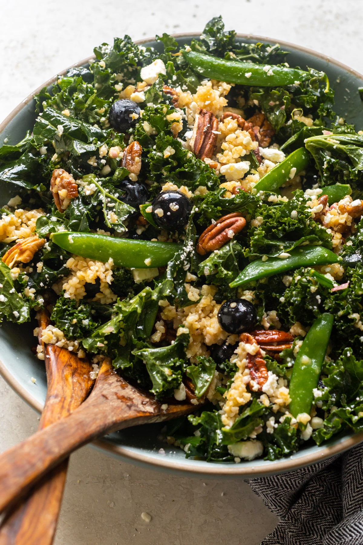 kale in a bowl with blueberries, pecans, bulgur wheat, feta cheese and dressing poured on top.