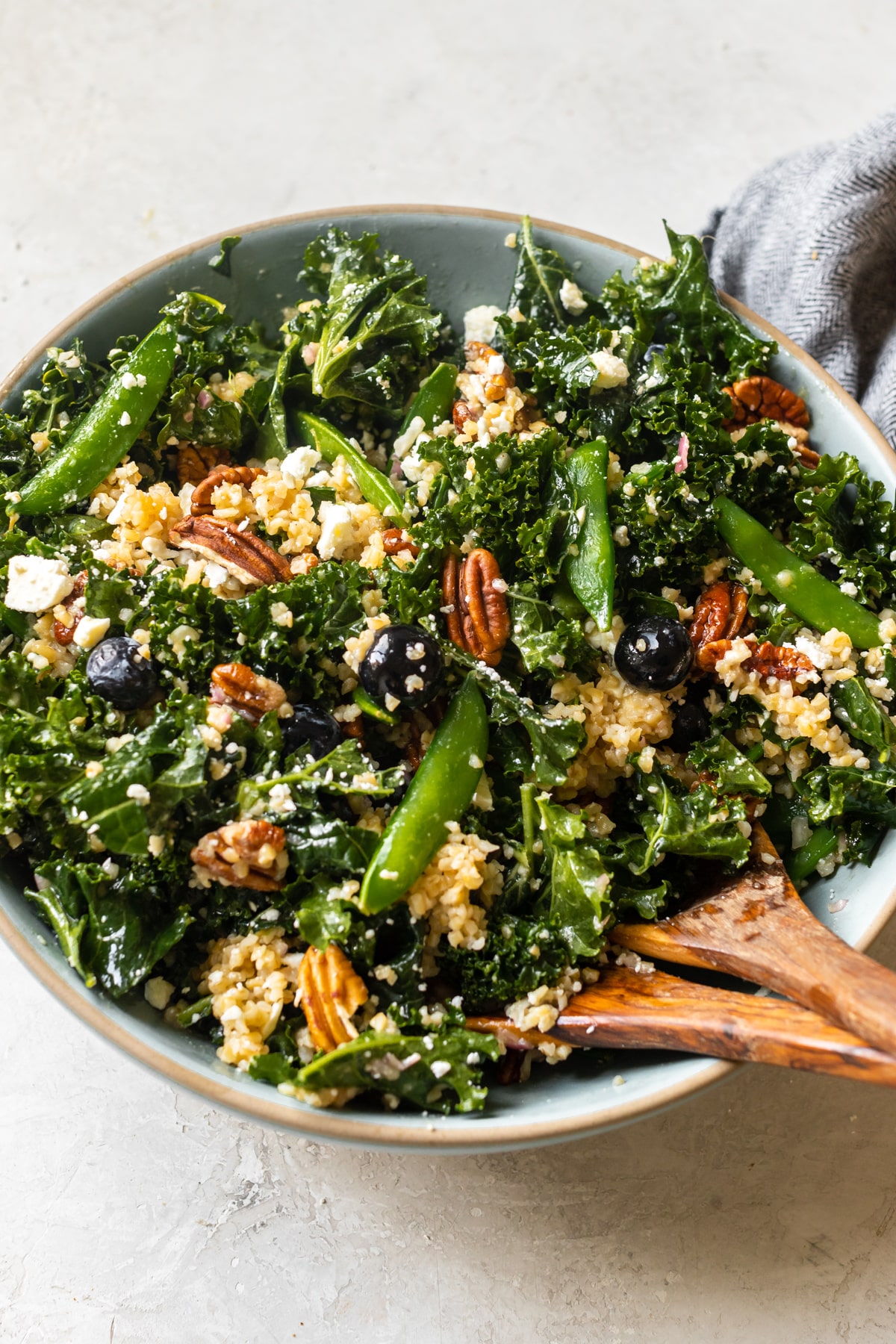 kale in a bowl with blueberries, pecans, bulgur wheat, feta cheese and dressing poured on top.