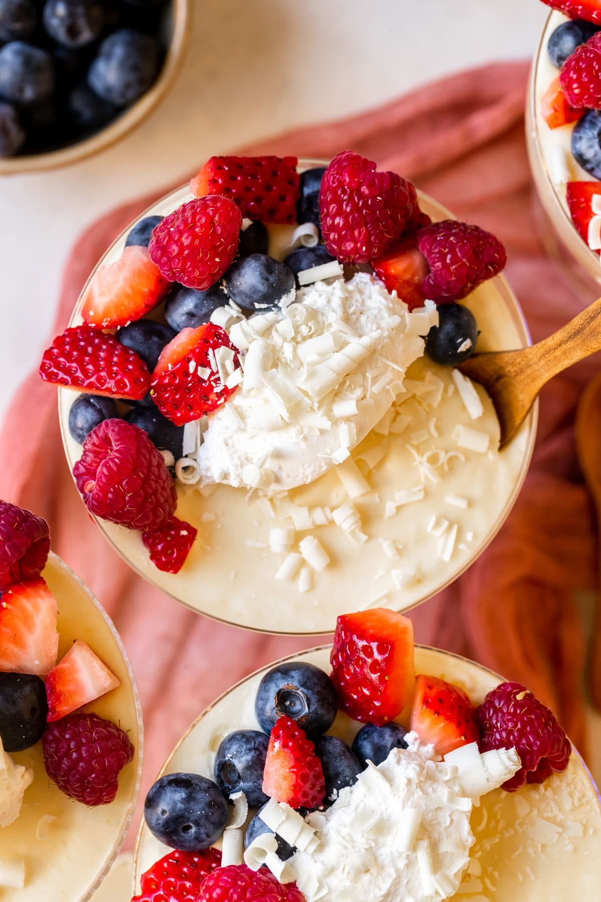mousse in martini glasses topped with whipped cream and fresh berries and white chocolate shavings.