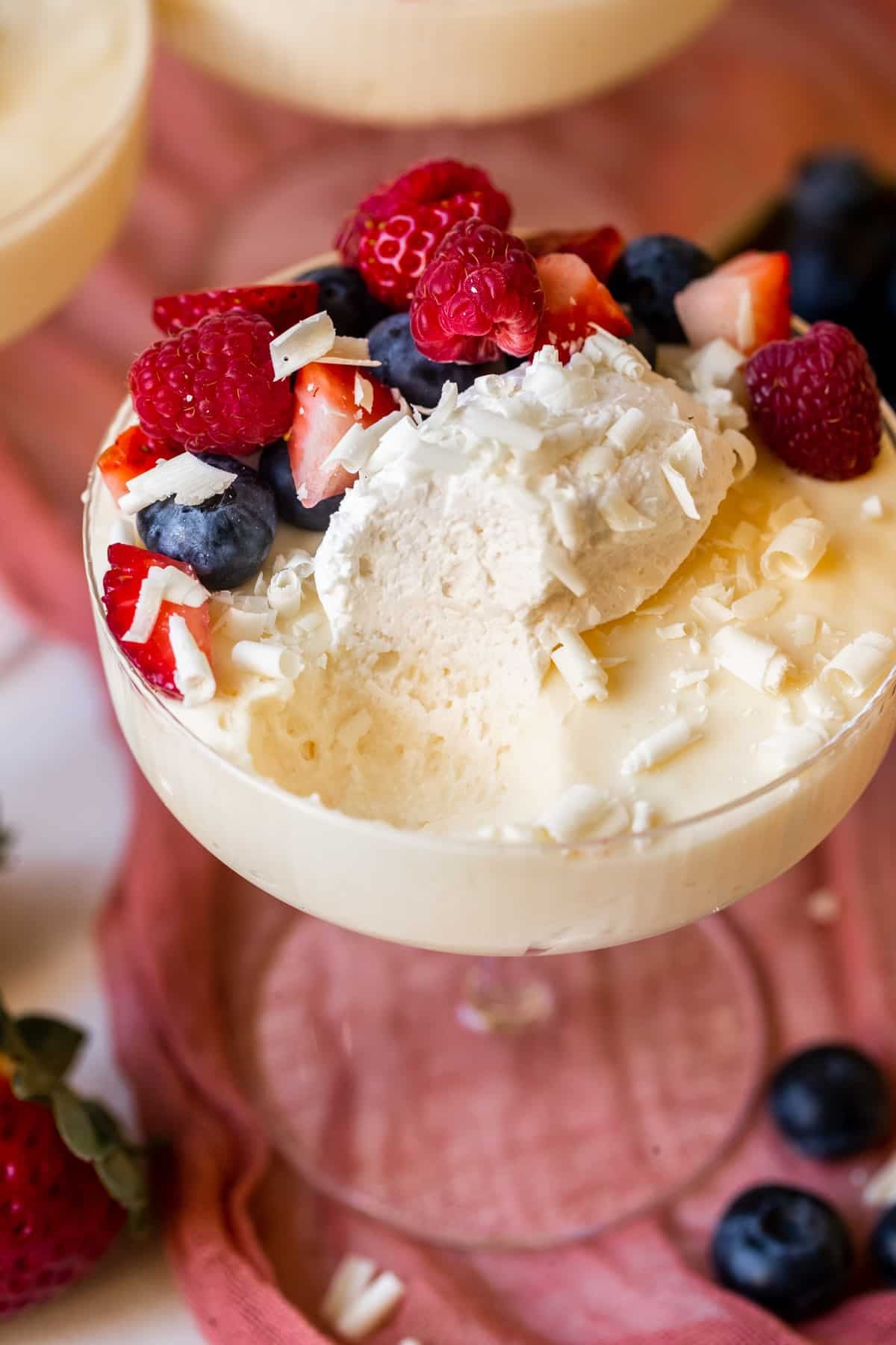 mousse in a martini glass with a bite taken out of it topped with whipped cream and fresh berries and white chocolate shavings.
