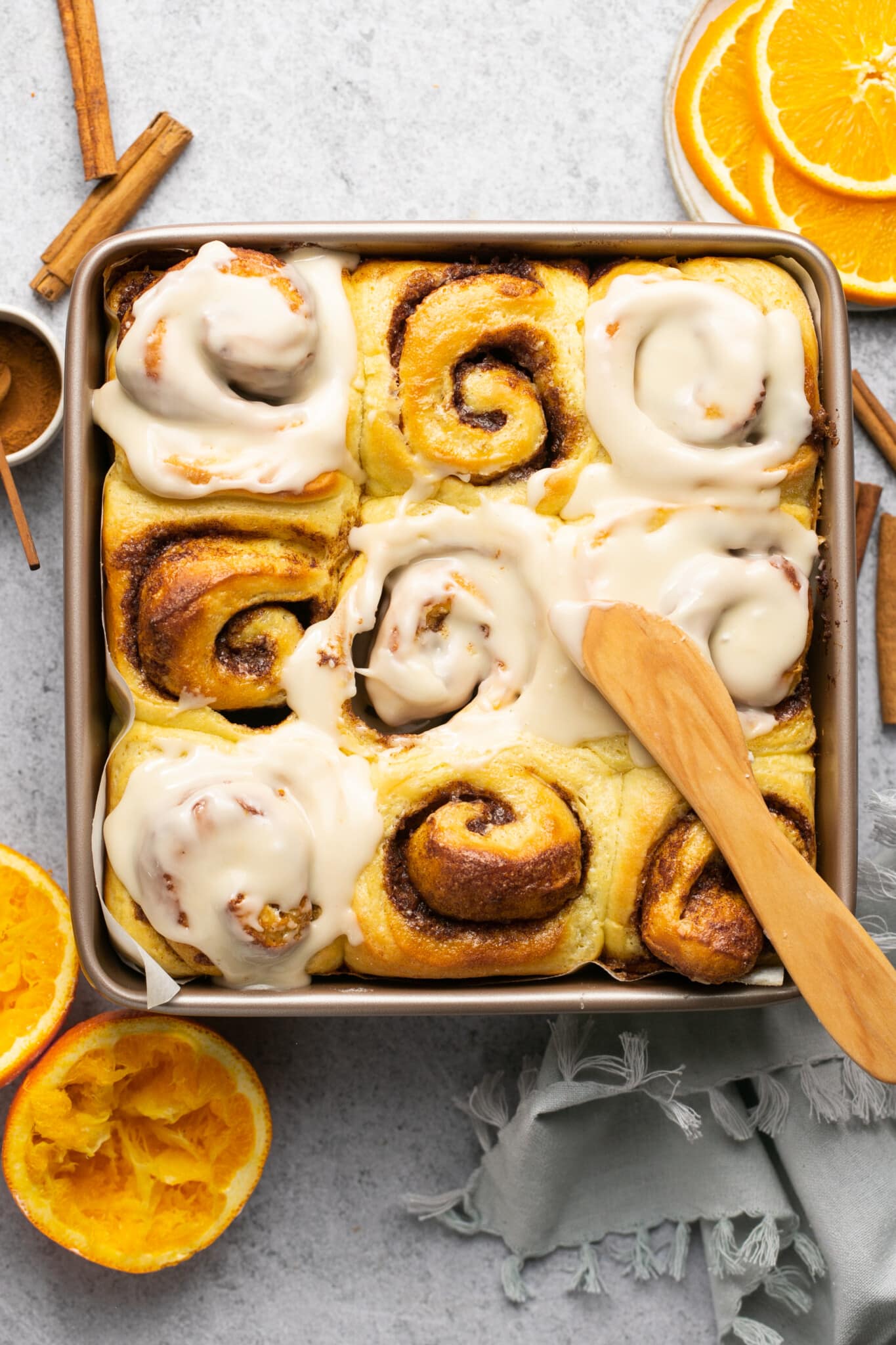baked orange cinnamon rolls with orange glaze being spread on top.