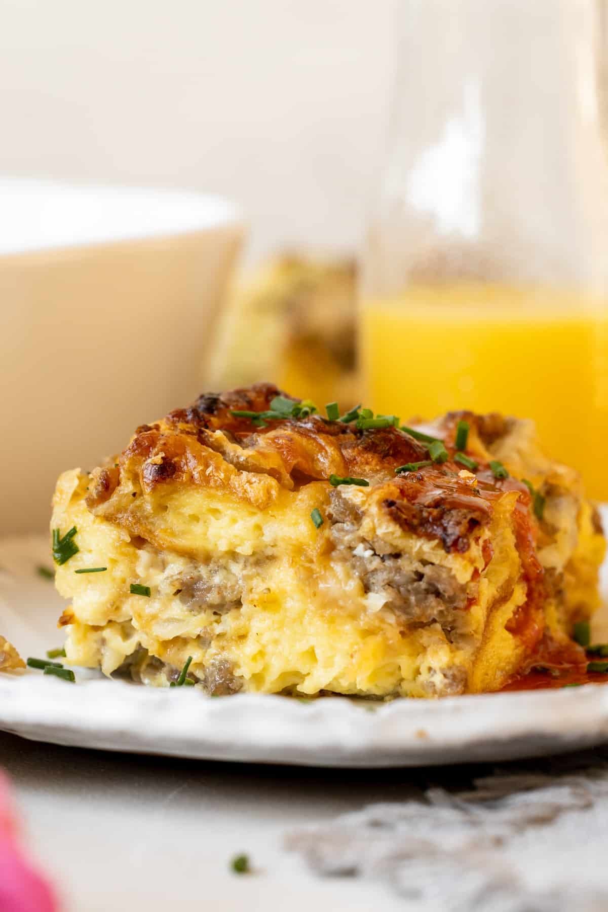 a slice of breakfast sausage casserole on a white plate garnished with chives. 
