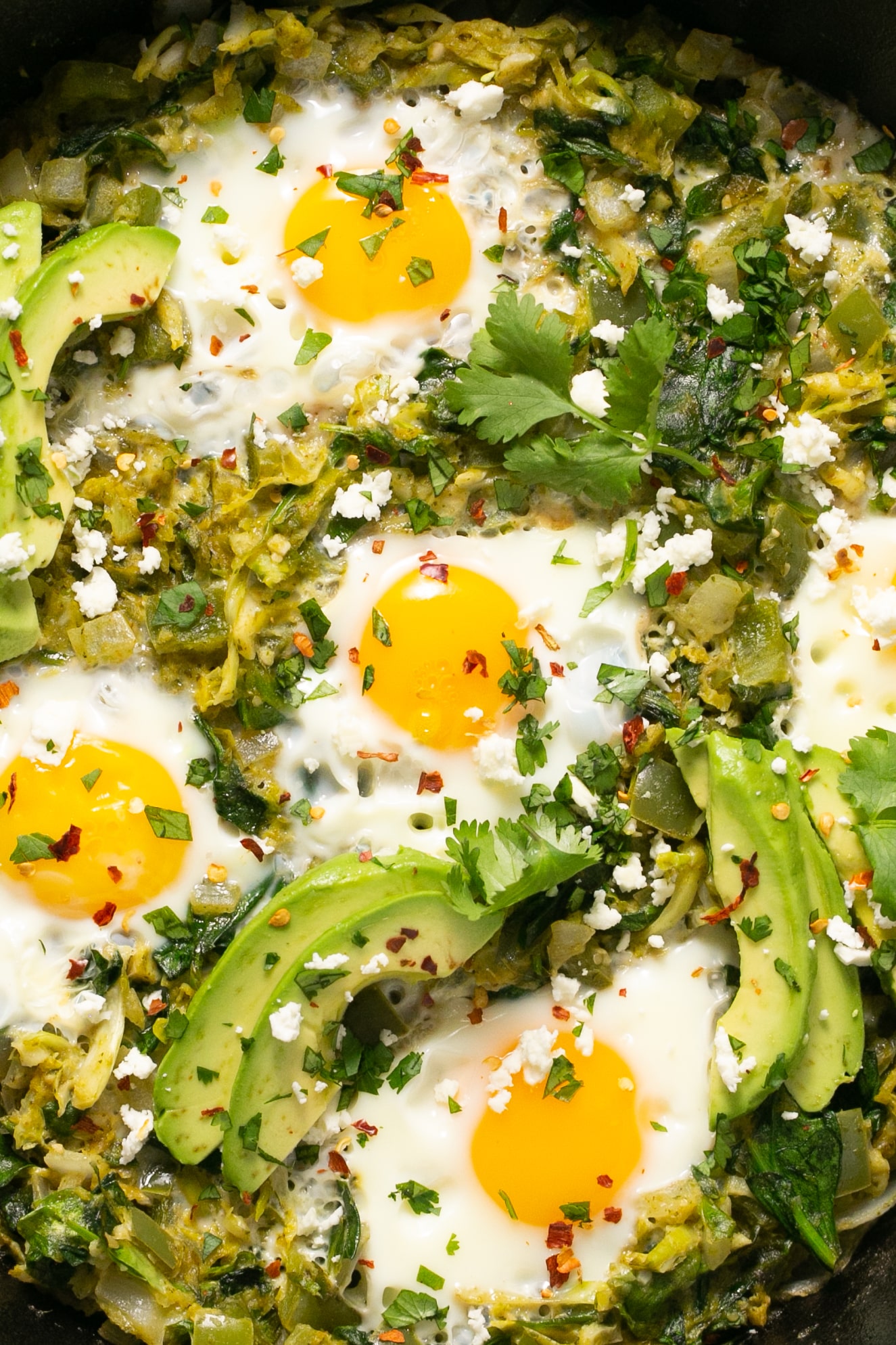 eggs in a skillet with veggies and avocado.